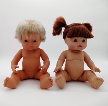 A Miniland doll sitting next to a Minikane doll