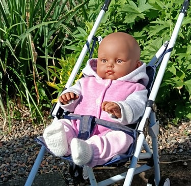Minikane doll Augustine outside in buggy wearing pink and grey jacket