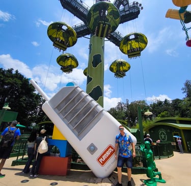 Hombre posando en la zona de Toy Story Land de Hong Kong Disneyland, con la atracción Toy Soldier Pa