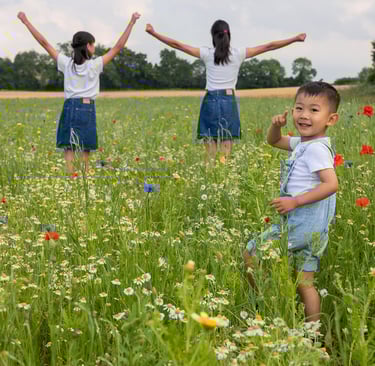 Young boy playing in a wildflower meadow with girls standing with arms raised in the background.