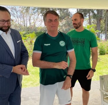 Jair Bolsonaro em pé, com camisa de futebol do Goiás, ao lado de dois homens.