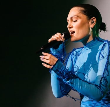 Jessie J cantando no palco, segurando um microfone e usando um traje azul.