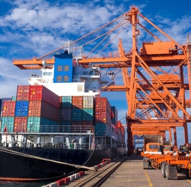Um navio cargueiro gigante ancorado em um porto com guindastes e caminhões.