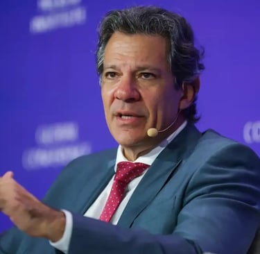  Fernando Haddad, de terno e gravata vermelha, em uma conferência, gesticulando com a mão.