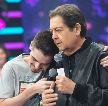Faustão abraça e segura um microfone com seu filho com uma camisa cinza