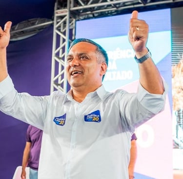 Marcelo Lima com uma camisa social branca, erguendo os polegares em um evento político.