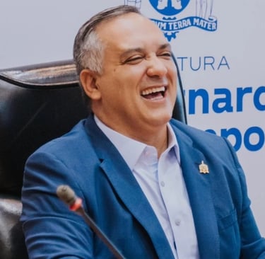 em um terno azul, sentado em uma cadeira, rindo.