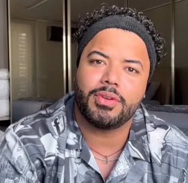 Hytalo em close, com um gorro preto, camisa estampada e barba.