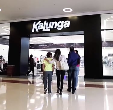  Família entra em uma loja da Kalunga em um shopping center, com outros clientes ao fundo.