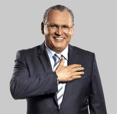Sidney Oliveira sorrindo em um terno azul, com a mão direita sobre o peito.