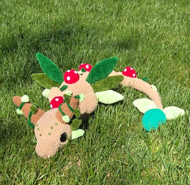 “Handmade crochet forest dragon plushie with antlers, felt leaves, and red mushroom details, resting