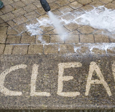 A man pressure washing with "clean" having been writen onto the sidewalk with the pressure washer