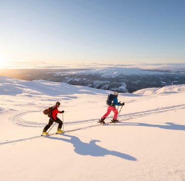 two people ski touring up the mountain during sunrise