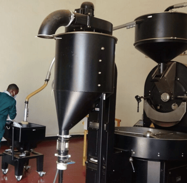 a man in a green uniform is standing in front of a coffee roasting machine