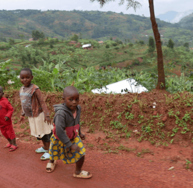 three children standing on a dirt road in their community