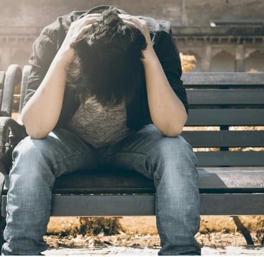 Vyras sėdintis parke ant suoliuko su nusileista galva, apimtas nerimo.