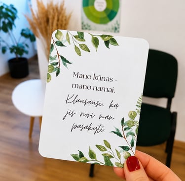 Afirmacijos kortelė, laikoma rankoje. Joje pateikiama afirmacija apie kūno priėmimą.