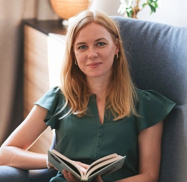 Psichologė Ieva Aukštuolytė sėdinti su knyga krėsle, šviesiame kambaryje..