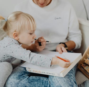 Vaikas su forne matoma mama piešia ant lapo, šalia pastatytos kaladėlės.