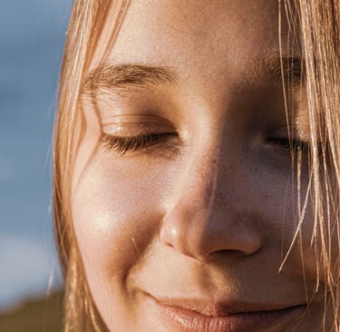 Moters veidas užmerktomis akimis, besišypsantis, apšviestas saulės, laimės ir ramybės akimirka