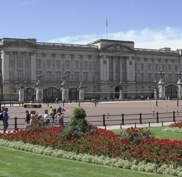 Exterior view of Buckingham Palace with vibrant flower beds in the foreground. 