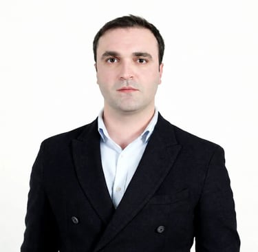 Professional headshot of a man in a black blazer and light blue shirt against a white background.