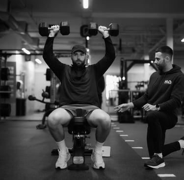 "Personal trainer guiding client through seated shoulder press in Leamington gym, focusing on form and support.