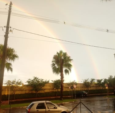 a rainbow - colored rainbow over a car parked in front of a fenced in