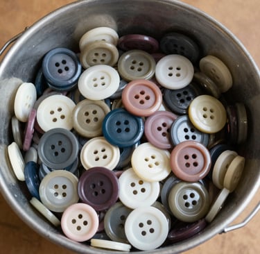A colorful sensory bin filled with dyed rice and large buttons scattered on top.