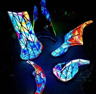 A night photo of the blooming sculpture with it's multi-colored art glass pannels illuminated