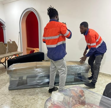 Two professional movers in orange high-visibility jackets with reflective strips collaborate to lift
