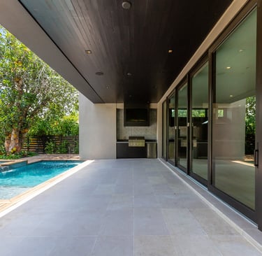 the outside patio of a luxury home with an outdoor grill, pool and deck with sliding glass doors