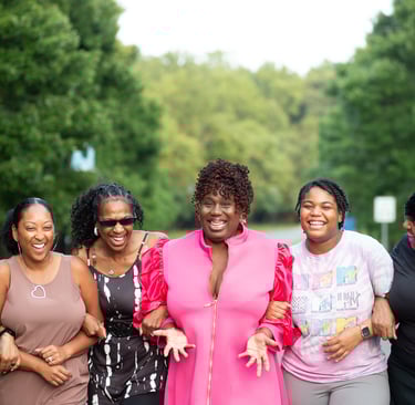a group of women standing around a woman in a pink dress smiling and looking happy