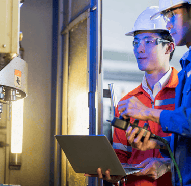 two men in hard hats and hard hats are standing in front of a machine