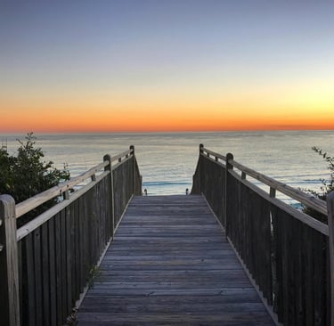 a wooden walkway leading to the beach at sunset