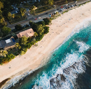 Aerial view of a tropical white sand beach with turquoise ocean waves crashing near coastal houses and a road.