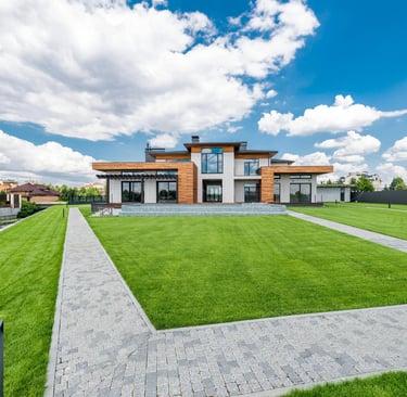 Modern luxury house with a manicured green lawn and stone walkway under a blue sky.