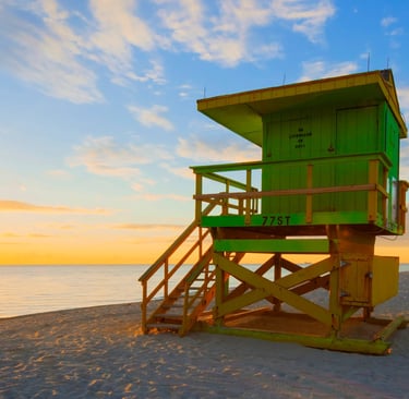 Sunrise over Miami Beach with a green lifeguard stand on the sandy shore and ocean horizon.