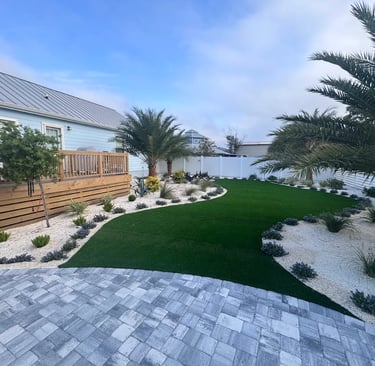 Modern backyard landscape with artificial turf, palm trees, and stone paver patio.