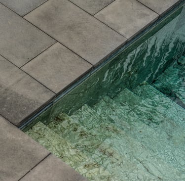 Modern luxury swimming pool with green natural stone tiles and gray concrete paver pool coping.