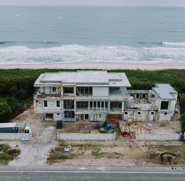 Aerial view of a luxury beachfront home under construction on a tropical coastline.