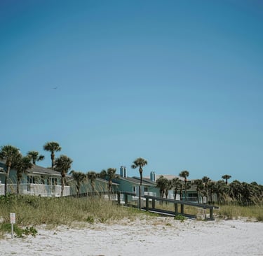 Luxury beachfront vacation rentals with palm trees and a wooden boardwalk on a sunny beach.