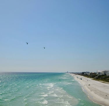 Two helicopters flying over turquoise ocean water and white sand beaches of a coastal resort town.