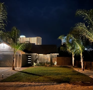Modern residential home at night with outdoor landscape lighting on palm trees and a green lawn.