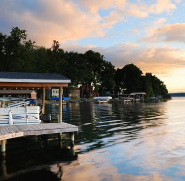 Sunset over a calm lake with boat docks, reflections, and lush green trees along the shoreline.