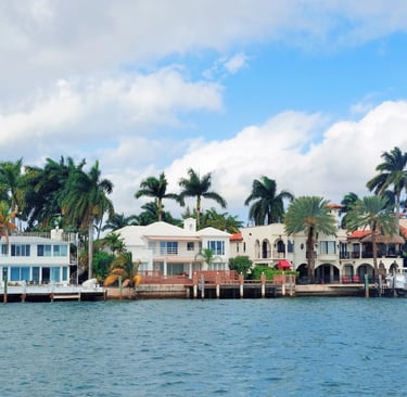 Luxury waterfront mansions in Miami Florida with palm trees and boat docks along the blue ocean water.