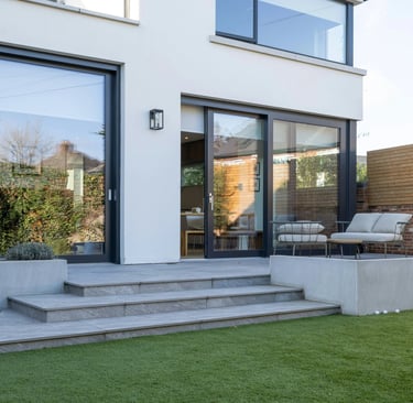 Modern home exterior with black sliding glass doors, stone patio steps, and artificial grass lawn.