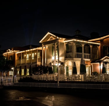Colonial-style buildings lit with warm string lights at night featuring an outdoor patio.