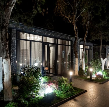 Modern glass cabin architecture with warm night lighting and landscaped garden pathway.