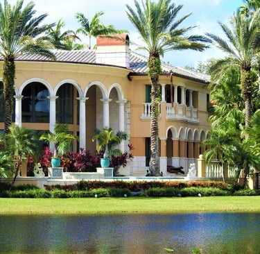 Luxury Mediterranean style waterfront mansion with arched windows and tropical palm trees.